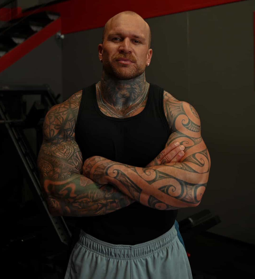 Man with tattoos standing in a dark indoor setting